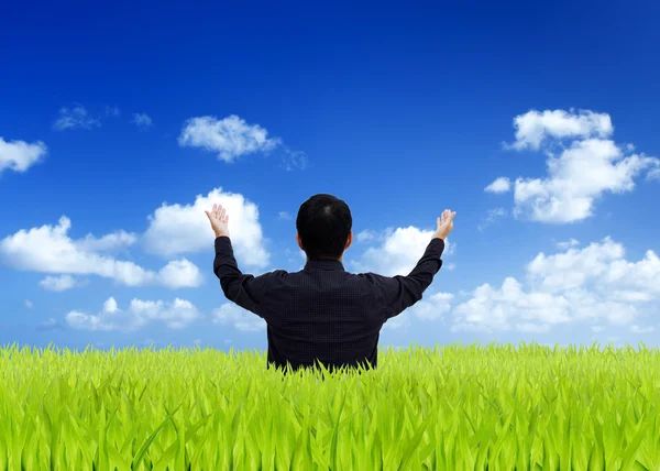 Man stretching out his hand on a green field with blue sky — Stock Photo, Image