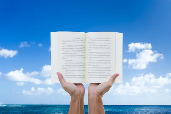 Uomo mano che tiene libro con mare e cielo blu sfondo — Foto Stock