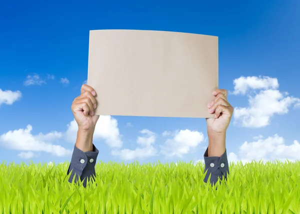Man hands holding blank cardboard on green field with blue sky background — Stock Photo, Image
