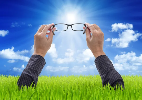 Hands holding eyeglasses with blue sky and green field backgroun — Stock Photo, Image