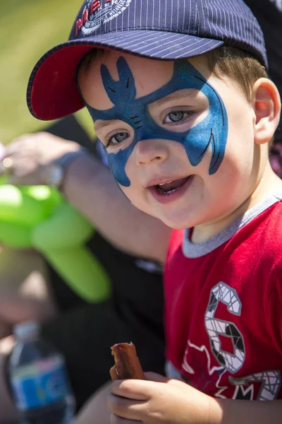 Young boy with blue face paint eating a hot dog Stock Image