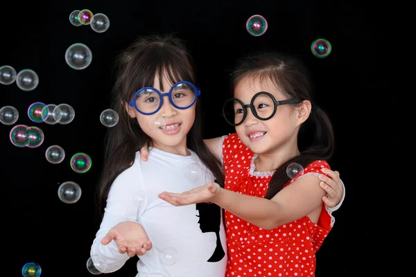 Dois menina feliz jogar com bolhas de sabão isolado fundo preto — Fotografia de Stock