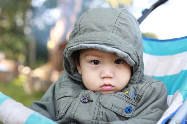 เด็กชายเอเชียตัวเล็กที่มีเสื้อโค้ทฤดูหนาวในรถเข็นเด็ก — ภาพถ่ายสต็อก