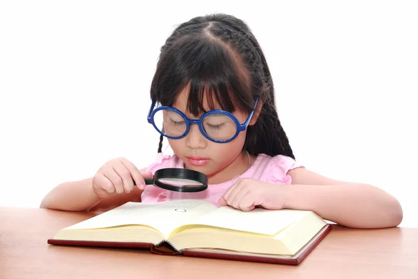 Азиатская девочка читает книгу с лупой — стоковое фото