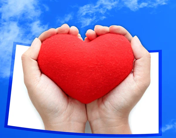 Red heart symbol on hands blue sky background — Stock Photo, Image