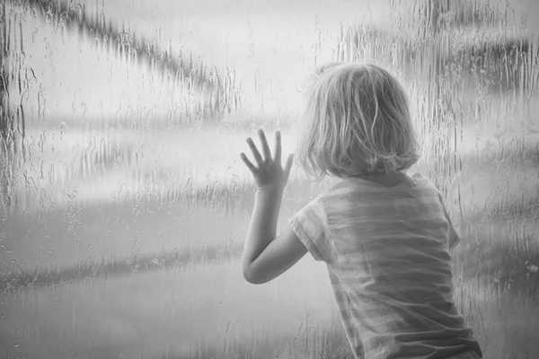 Девочка смотрит на капли дождя на окне — стоковое фото