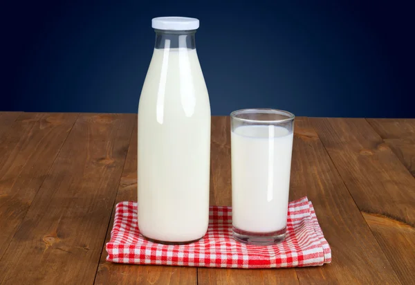 Botella llena de leche fresca y un vaso es mesa de madera sobre un fondo azul Fotos de stock