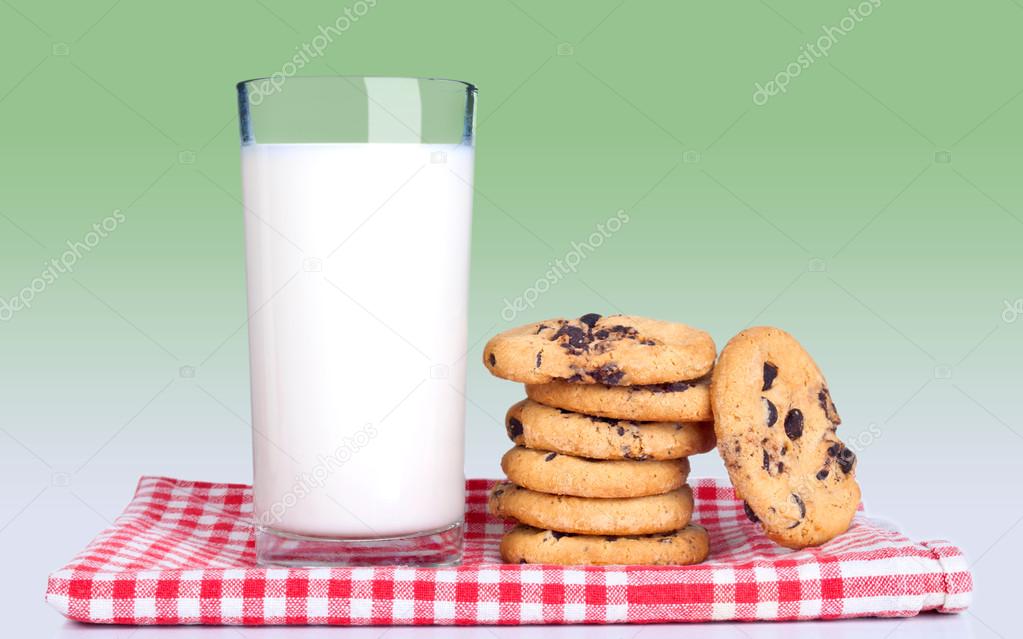 Glass of milk and cookies on kitchen towel with red cells isolated on green background