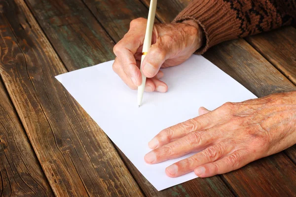 Närbild av äldre manliga händer på träbord. skriva på blankt papper Stockbild