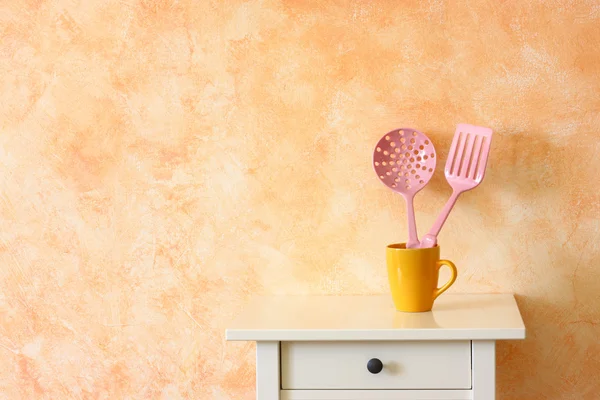 Kitchen cooking utensils. plastic spatulas in yellow cup against rustic terracotta wall. — Stock Photo, Image