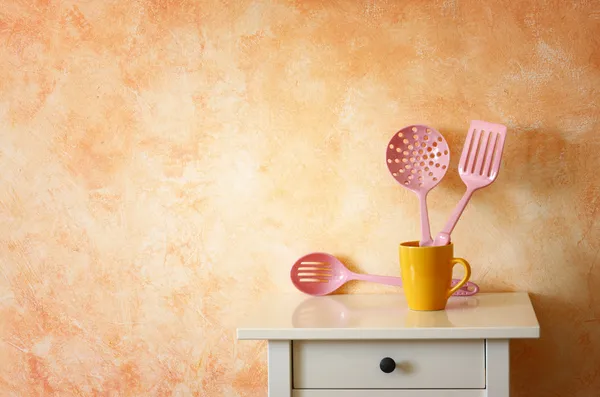 Ustensiles de cuisine. spatules en plastique dans une tasse jaune contre une paroi rustique en terre cuite . — Photo