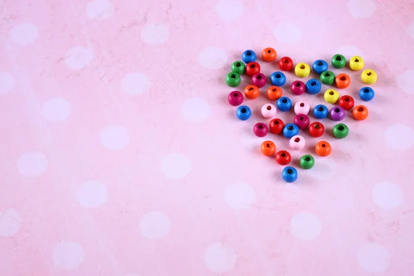 Forma de coração colorido feito de contas no fundo do vintage rosa — Fotografia de Stock
