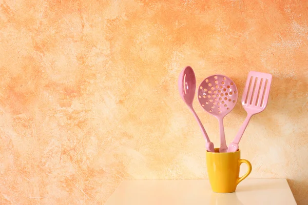 Kitchen cooking utensils. plastic spatulas in yellow cup against rustic terracotta wall — Stock Photo, Image