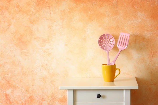 Kitchen cooking utensils. plastic spatulas in yellow cup against rustic terracotta wall. — Stock Photo, Image