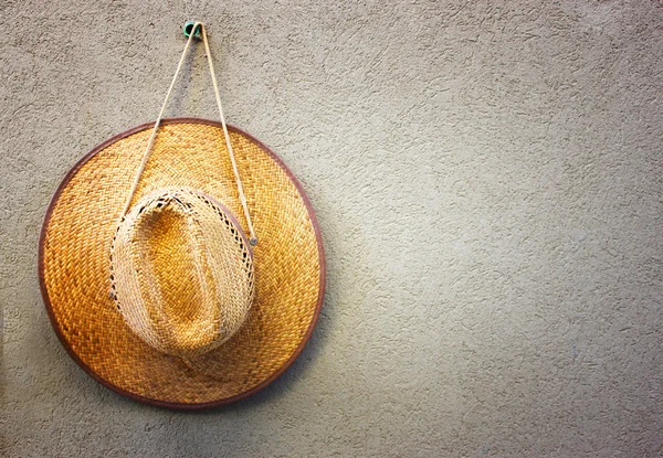 Chapeau de paille accroché sur un mur texturé — Photo