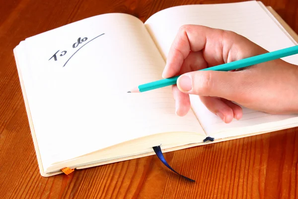 Mujer mano sosteniendo lápiz y abrió cuaderno con una lista de cosas que hacer . —  Fotos de Stock