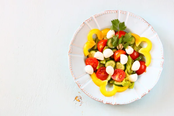 Salade met mozzarella en verse groenten op houten tafel achtergrond. — Stockfoto