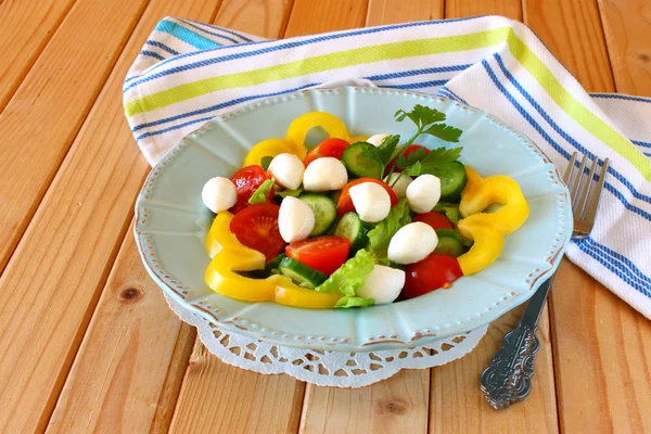 Salad with mozzarella and fresh vegetables on wooden table background. — Stock Photo, Image