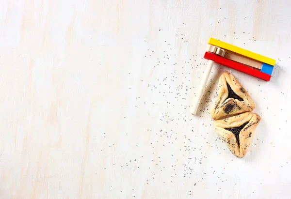 Hamantaschen cookies of hamans oren voor purim viering en noisemaker over getextureerde houten bord — Stockfoto