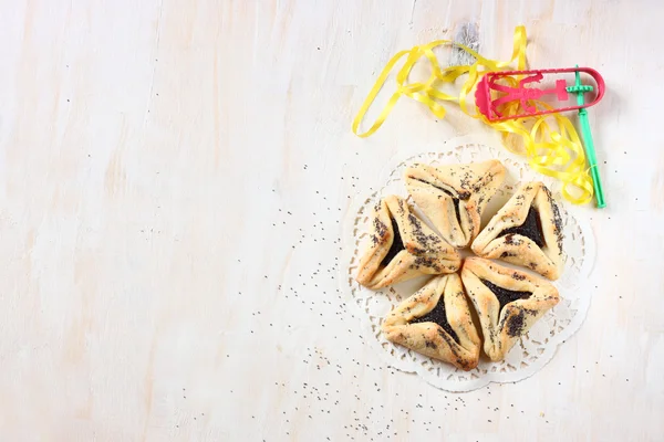 Hamantaschen cookies or hamans ears for Purim celebration and noisemaker over textured wooden board — Stock Photo, Image
