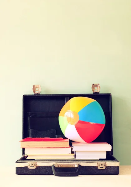 Open case with books and beach ball. vacation or travel concept.