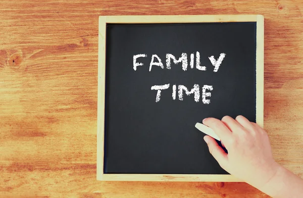 Kid hand holding chalk and writing family time over blackboard. top view. — Stock Photo, Image