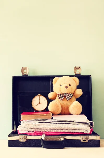 Open case with books towel teddy bear and vintage clock. vacation concept. — Stock Photo, Image