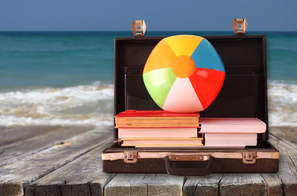 Open briefcase with books and beach ball. sea in the background