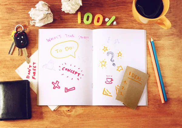 Top view of messy table with notebook with doodles, coffee cup, papers and keys. — Stock Photo, Image