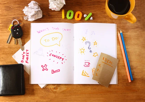 Top view of messy table with notebook with doodles, coffee cup, papers and keys. — Stock Photo, Image