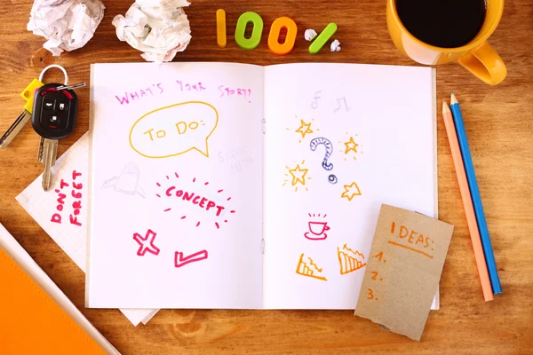 Top view of messy table with notebook with doodles, coffee cup, papers and keys. — Stock Photo, Image