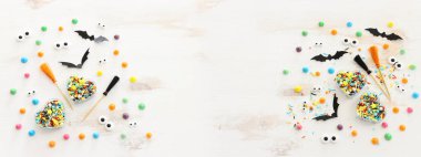 Cadılar Bayramı sanal gününün en üst görüntüsü. Beyaz ahşap masa üzerinde cadı süpürgesi, ikram ve yarasalar