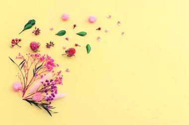 Sarı arkaplan üzerinde pembe, mor ve yeşil çiçek kompozisyonu üst görünüm .Düz yatıyordu