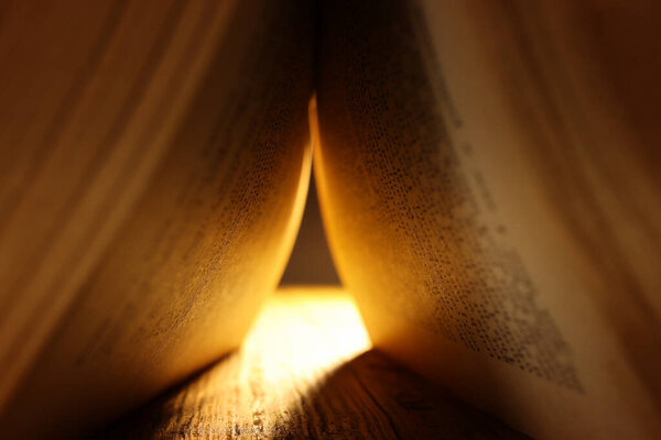 Image of open antique book on wooden table with bright light
