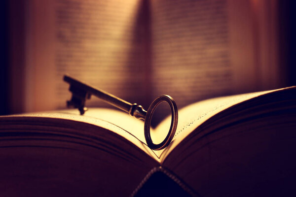 Image of open antique book on wooden table with vintage key