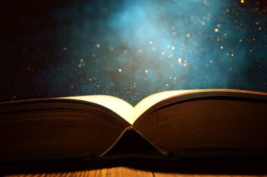 Tahta masanın üzerinde parıltılı kaplamalı açık antik kitap görüntüsü