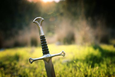 Gümüş kılıcın gizemli ve sihirli fotoğrafı İngiltere ormanları üzerinde ya da parlayan bir arazi üzerinde. Ortaçağ konsepti.