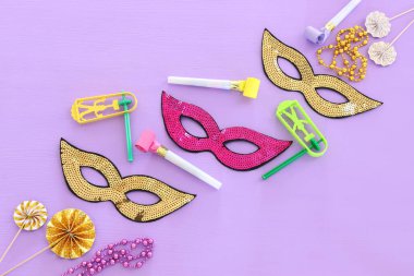 Mor ahşap arka planda parti maskeleri ve gürültü çıkarıcı. Üst manzara, düz uzanma