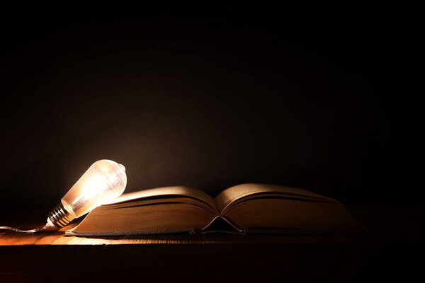 Image of open antique book and lamp on wooden table with dark background