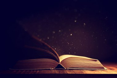 Tahta masanın üzerinde parıltılı kaplamalı açık antik kitap görüntüsü