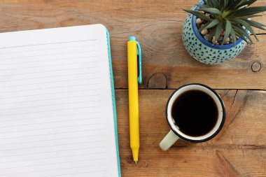 Üzerinde boş sayfalar ve ahşap masanın üzerinde bir fincan kahve olan açık defter görüntüsü. Metin ya da model eklemeye hazır.