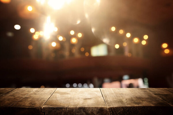 Изображение деревянного стола перед размытыми огнями ресторана