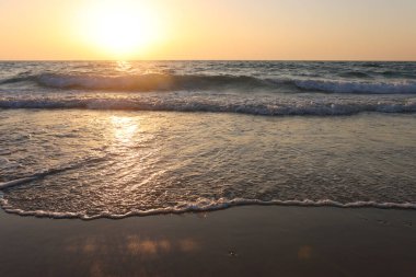 Deniz dalgaları ve ılık gün batımı ışığı, sakin ve rahatlatıcı kumsal