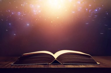 Tahta masanın üzerinde parıltılı kaplamalı açık antik kitap görüntüsü