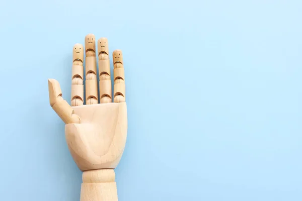 Wooden figure hand with happy faces on blue background.