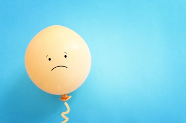 Mavi arka planda üzgün yüzlü balon görüntüsü. Duygu, üzüntü ya da stres kavramı