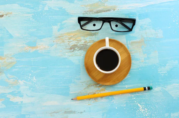 Top view image of coffee cup and glasses as funny face over blue wooden table. Happiness and joy concept