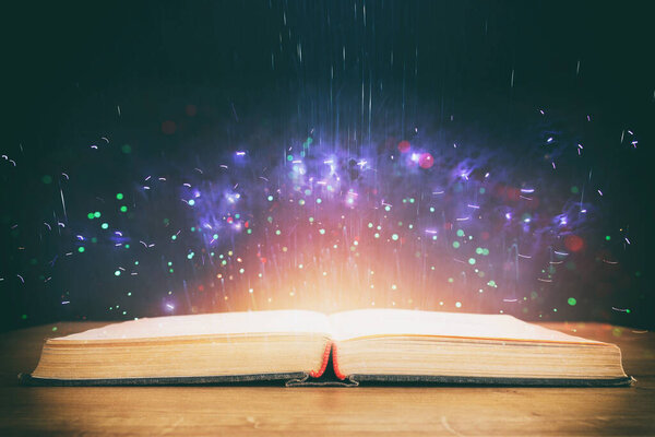 Image of open antique book on wooden table with glitter overlay