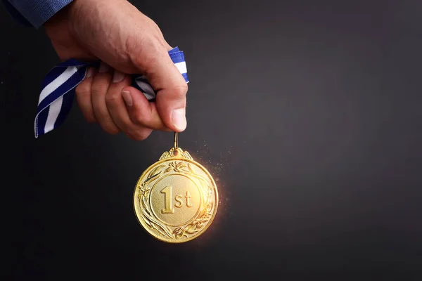 Male hand holding golden medal over dark background and light burst