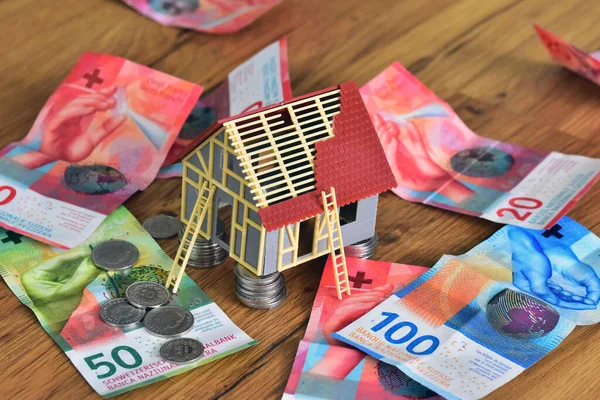 house under construction with swiss money banknotes and coins